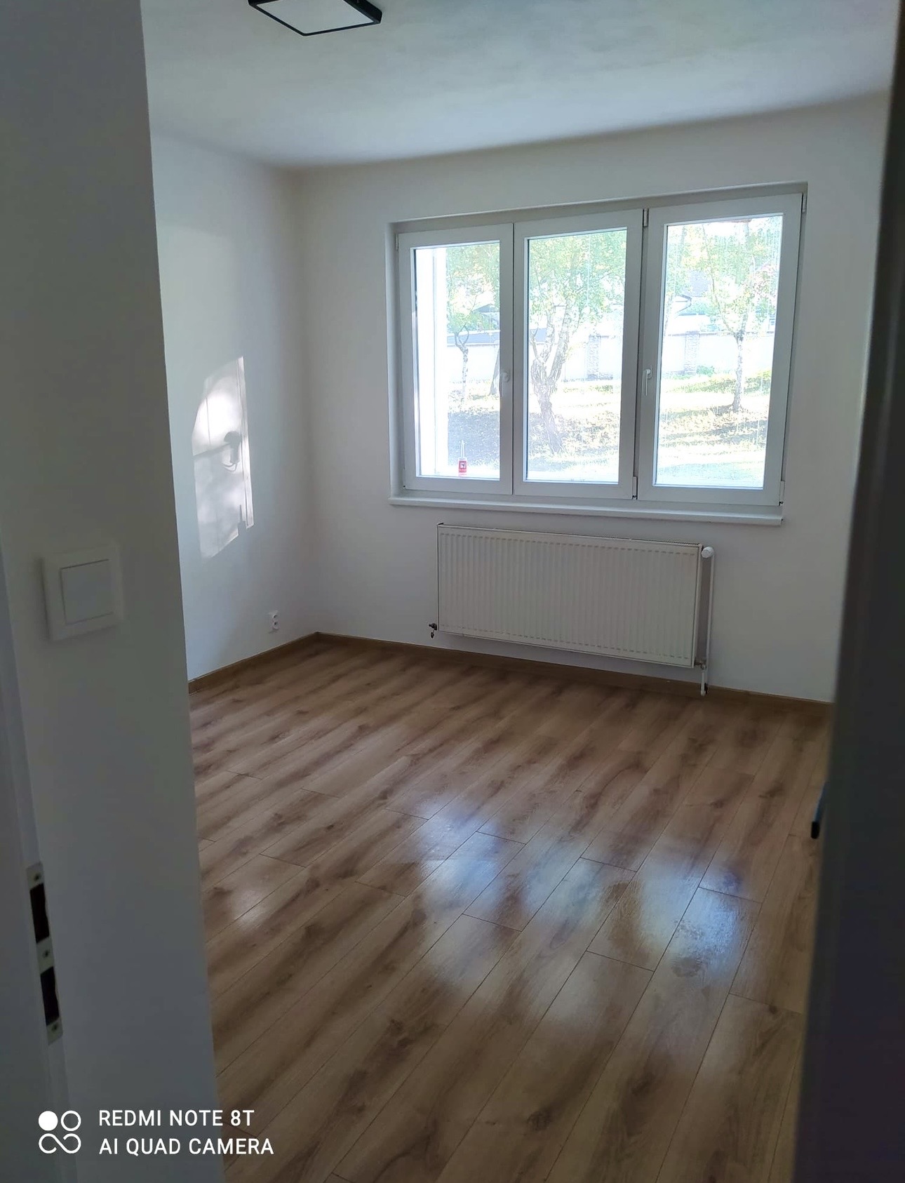 Vymalovaný pokoj s dřevěnou podlahou a velkým oknem
